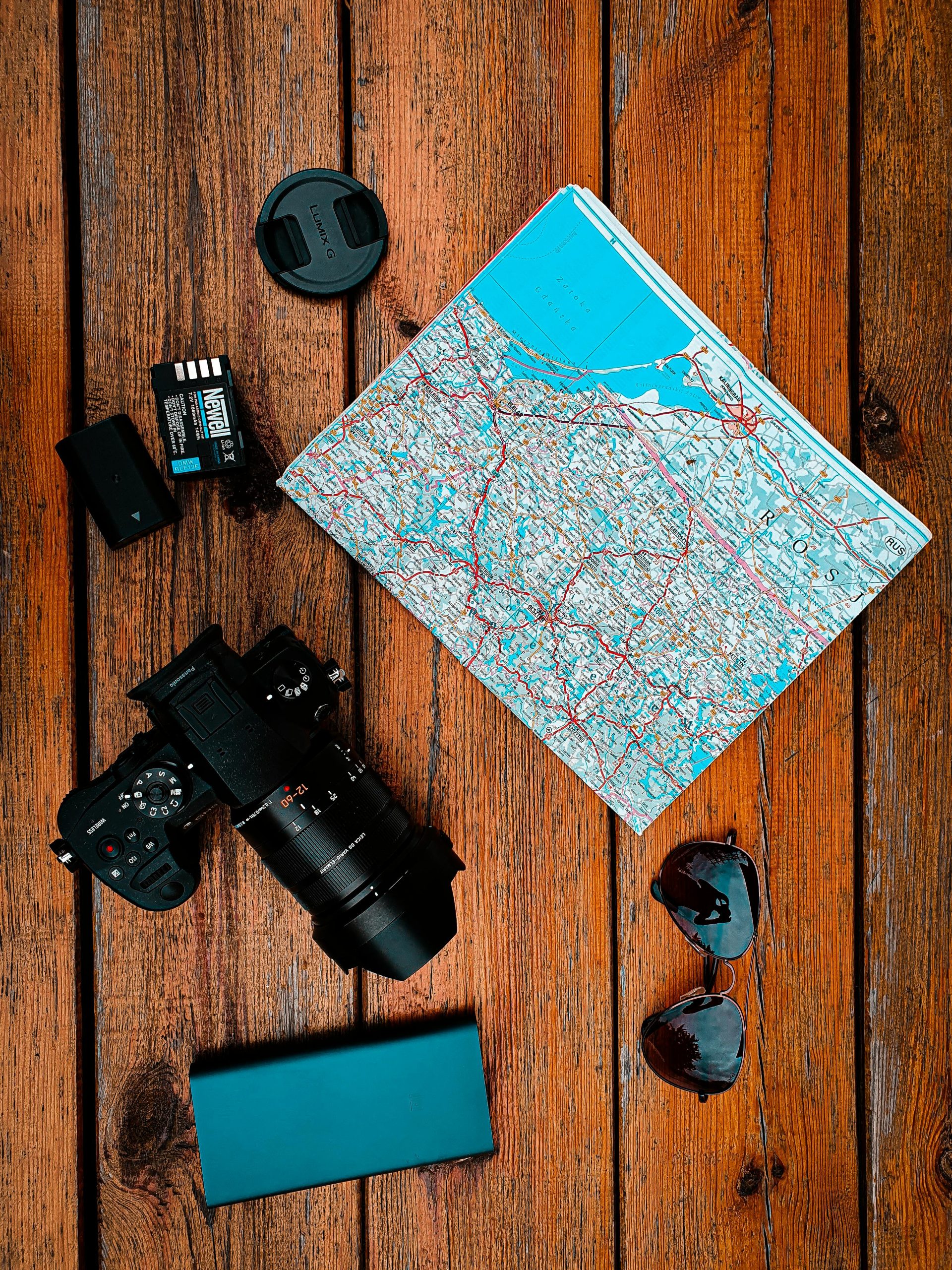 Flat lay of travel gear including camera, map, and sunglasses on wooden surface.